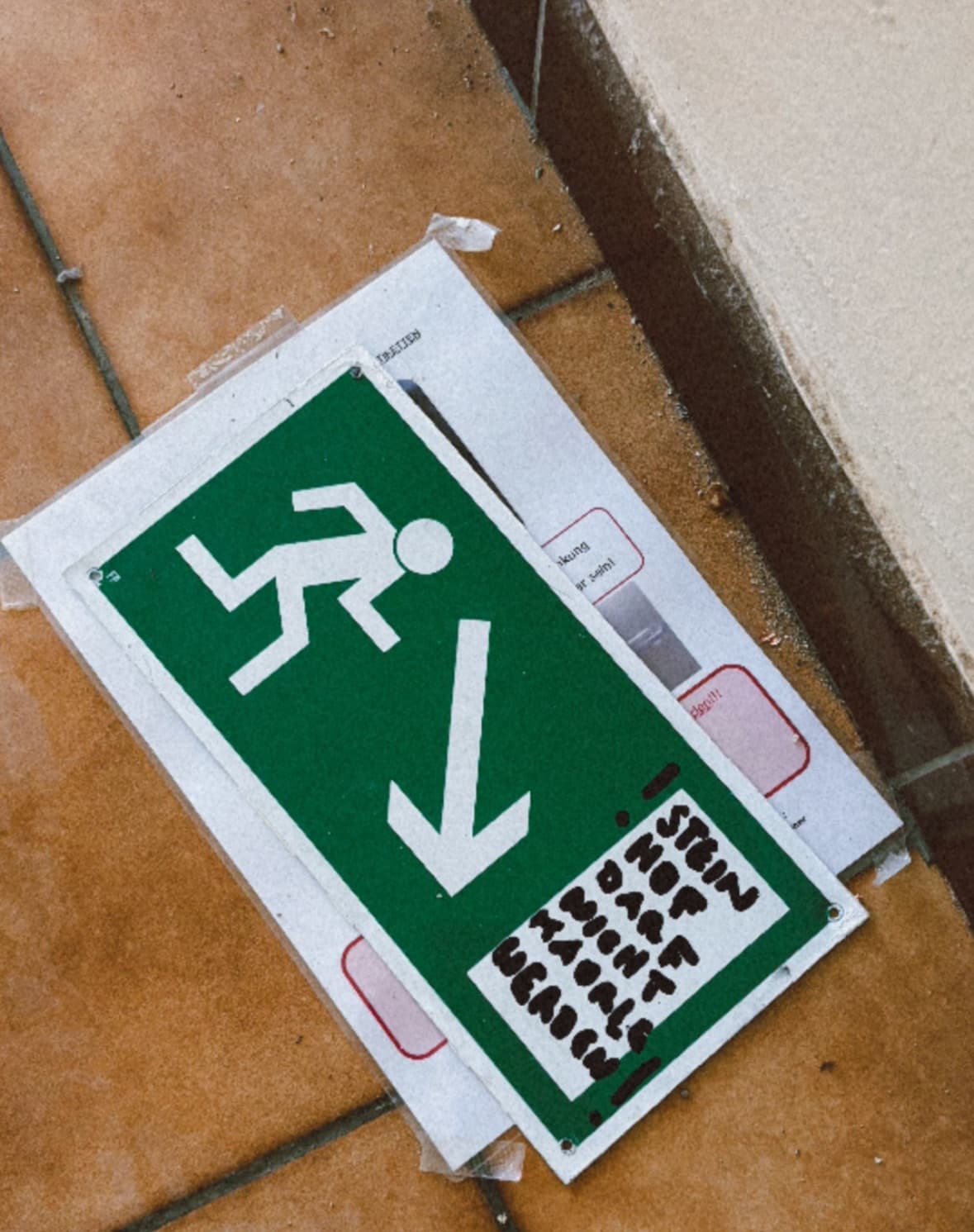 Ein grünes Fluchtwegsschild auf dem Fliesenboden auf welches mit Edding